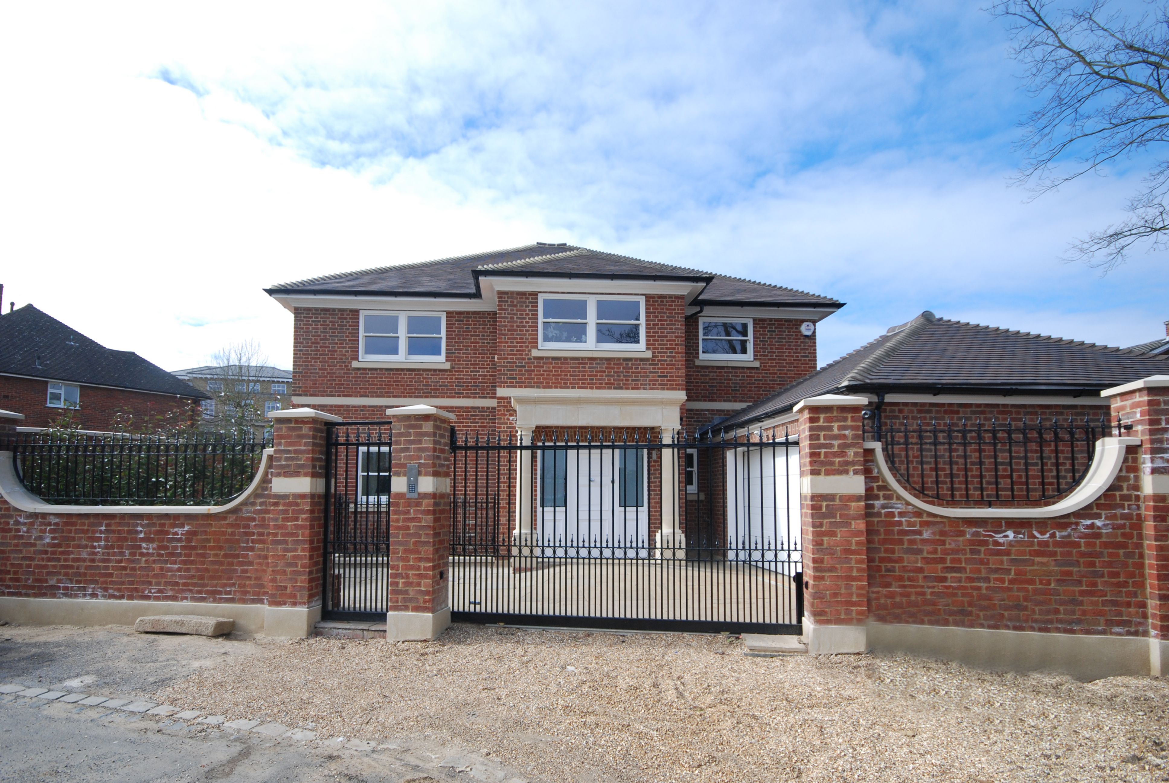 Exterior front elevation of the brick house with electric gates and stone piers